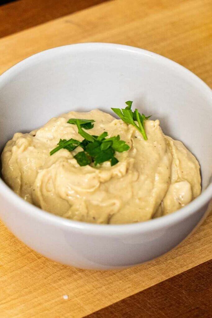 close up of miso tahini dressing in a white bowl topped with a green garnish