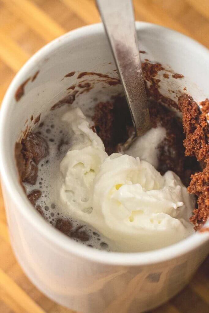 close up of vegan mug brownie with spoon and whipped cream