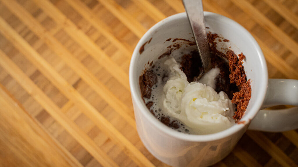 vegan brownie in a white mug with spoon and whipped cream