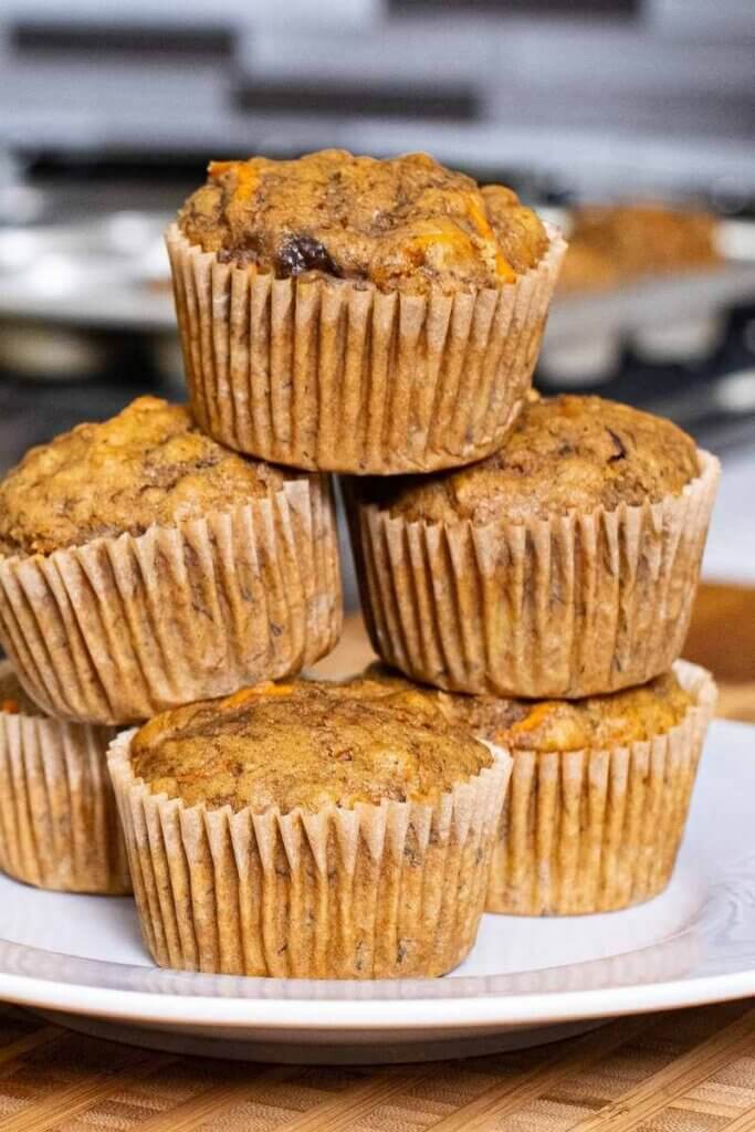 side shot of banana carrot muffins stacked on top of each other on a white plate