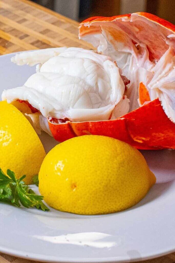 side shot of instant pot lobster on white plate with lemon wedges