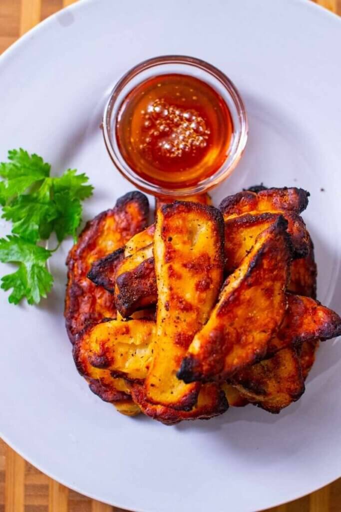 top shot of baked halloumi fries on white plate next to ramekin of sauce