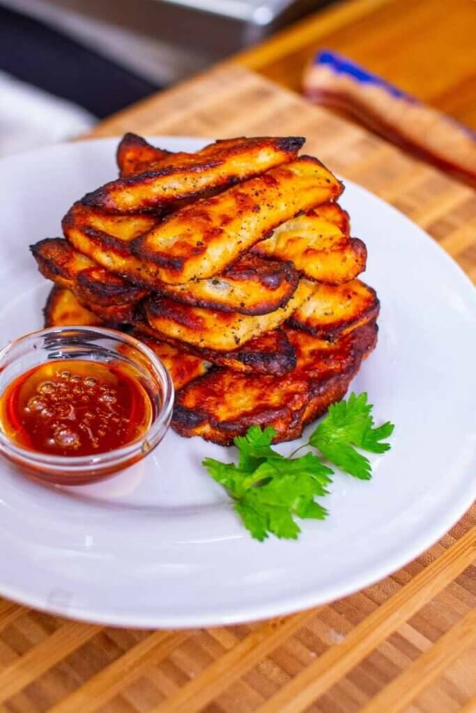 side view of halloumi fries stacked on a plate next to sauce