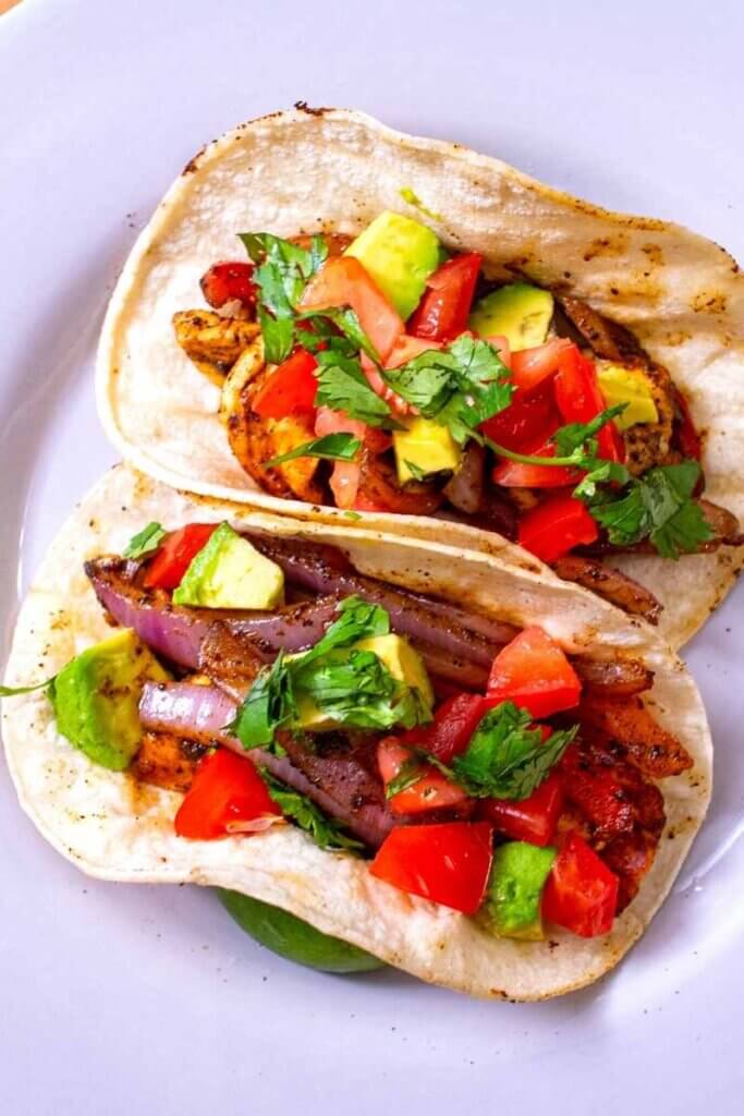 two halloumi chicken fajitas in corn tortillas on a plate next to lime wedge