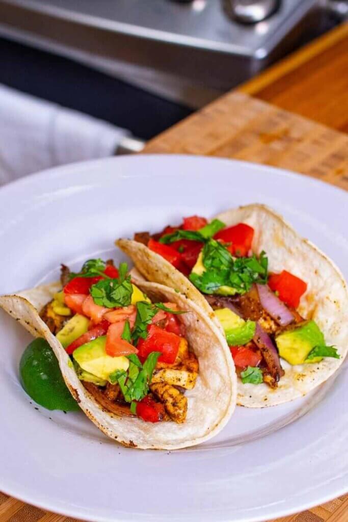side shot of two chicken and halloumi fajitas on a plate with lime wedge