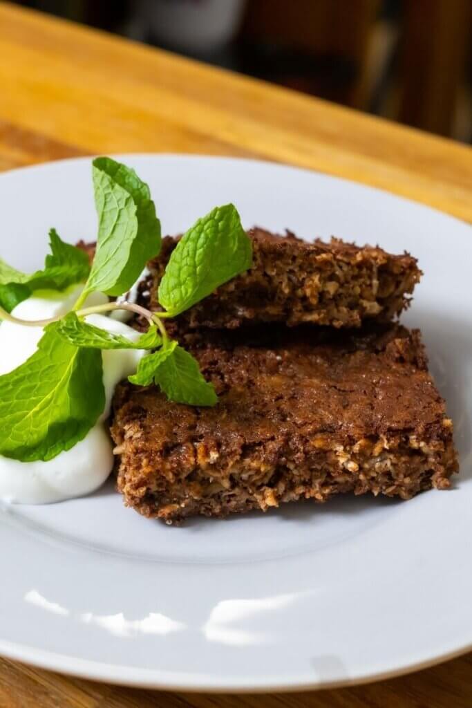 two chocolate baked oat bars on white plate next to garnish