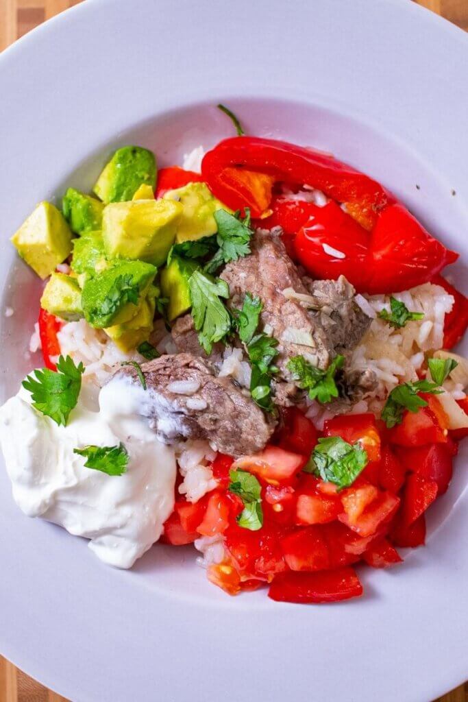 top view of oven steak fajitas in a white bowl with toppings