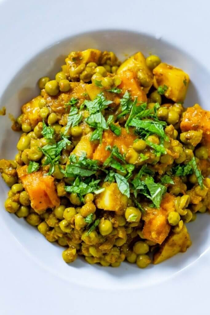 top view of green peas curry in a large white bowl with veggies
