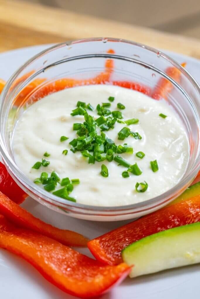 vegan horseradish sauce in a glass bowl on a plate with peppers