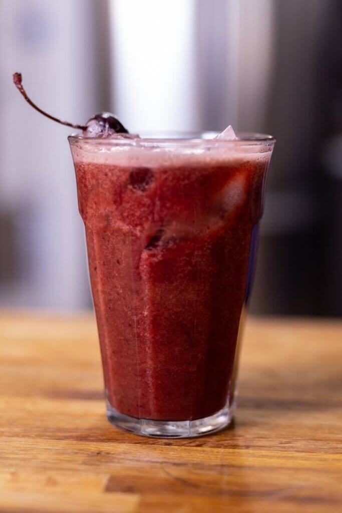 side view of a homemade cherry cooler garnished with a cherry