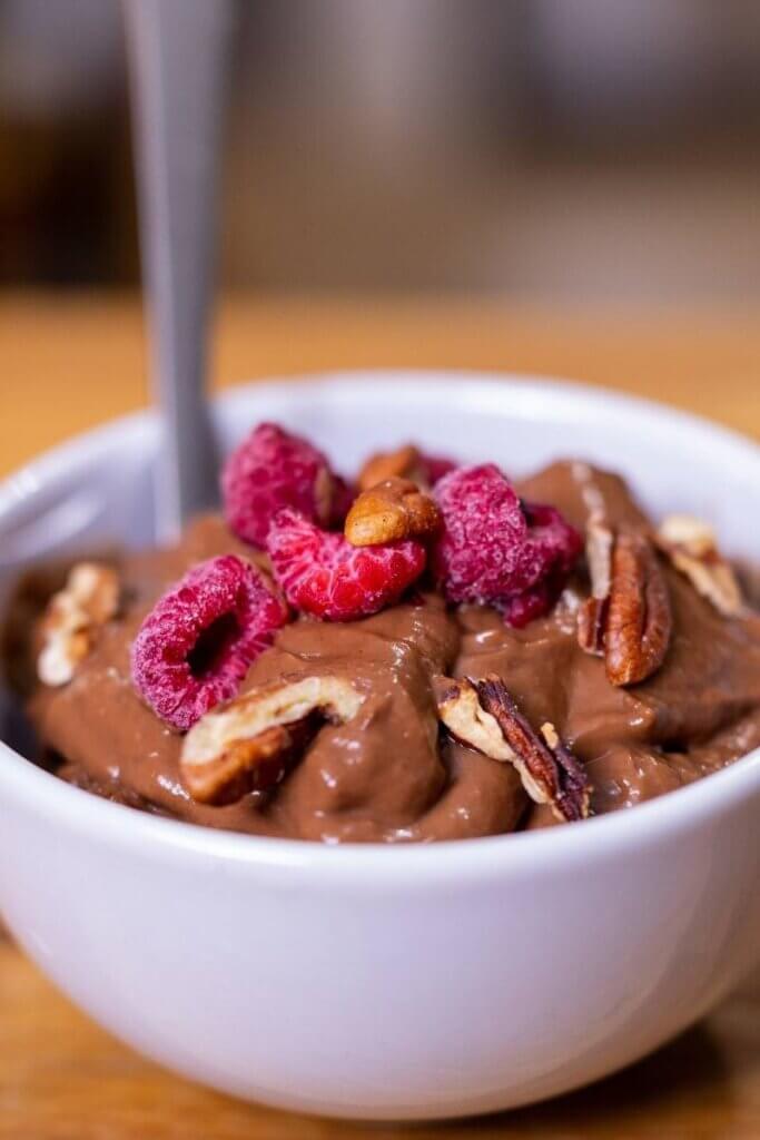 homemade oat milk chocolate pudding in a white bowl with pecans and raspberries