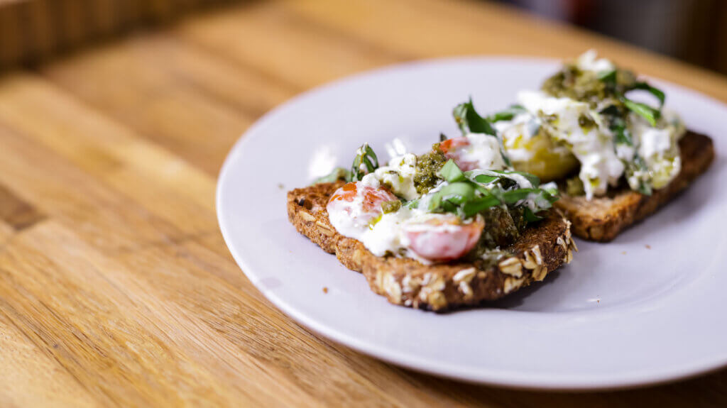 two pieces of burrata pesto toast on a white plate