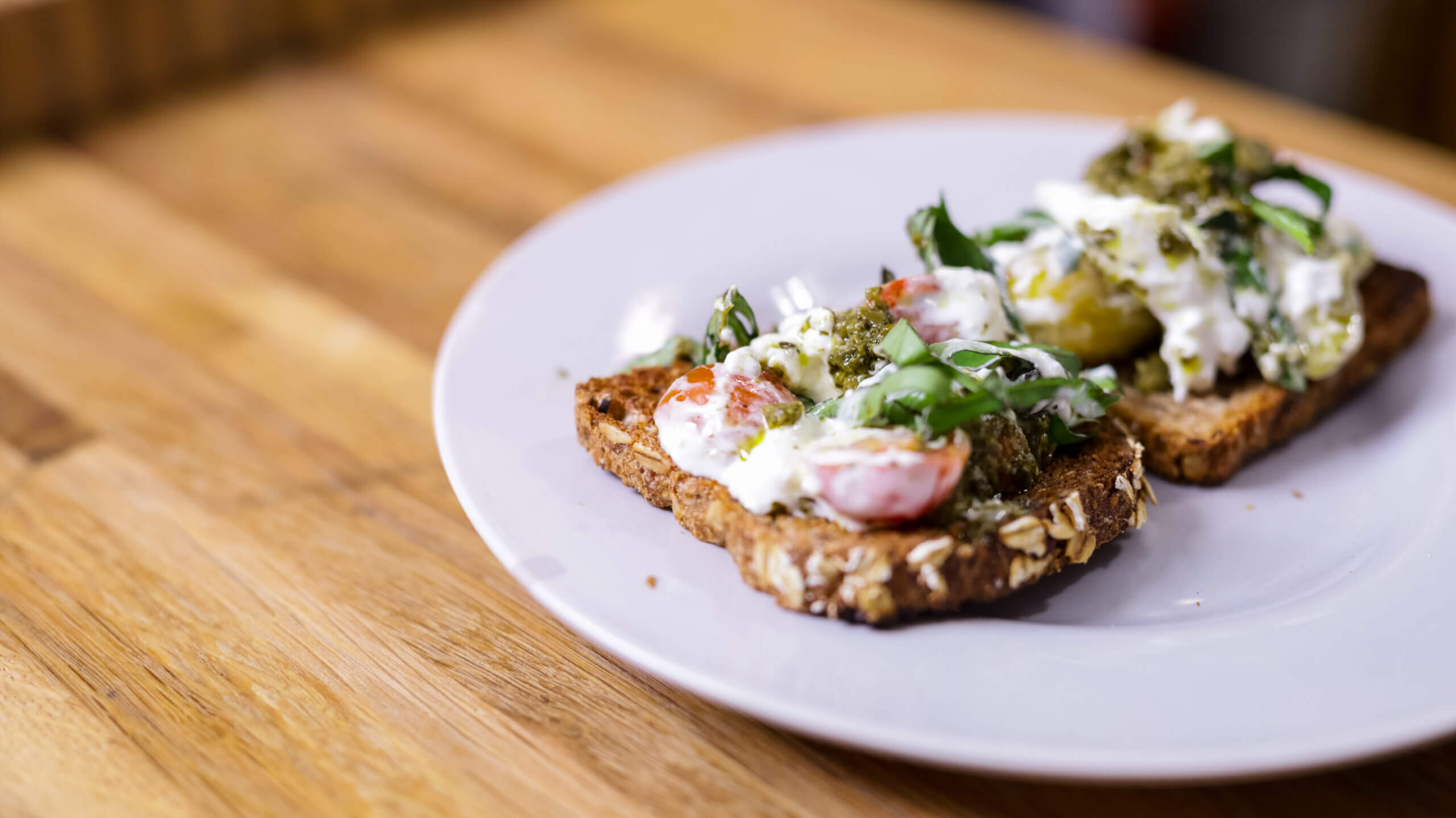 two pieces of burrata pesto toast on a white plate
