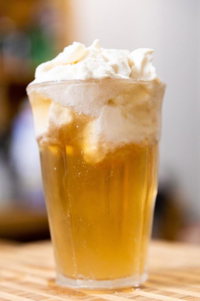 side view of alcoholic butterbeer topped with whipped cream in a glass