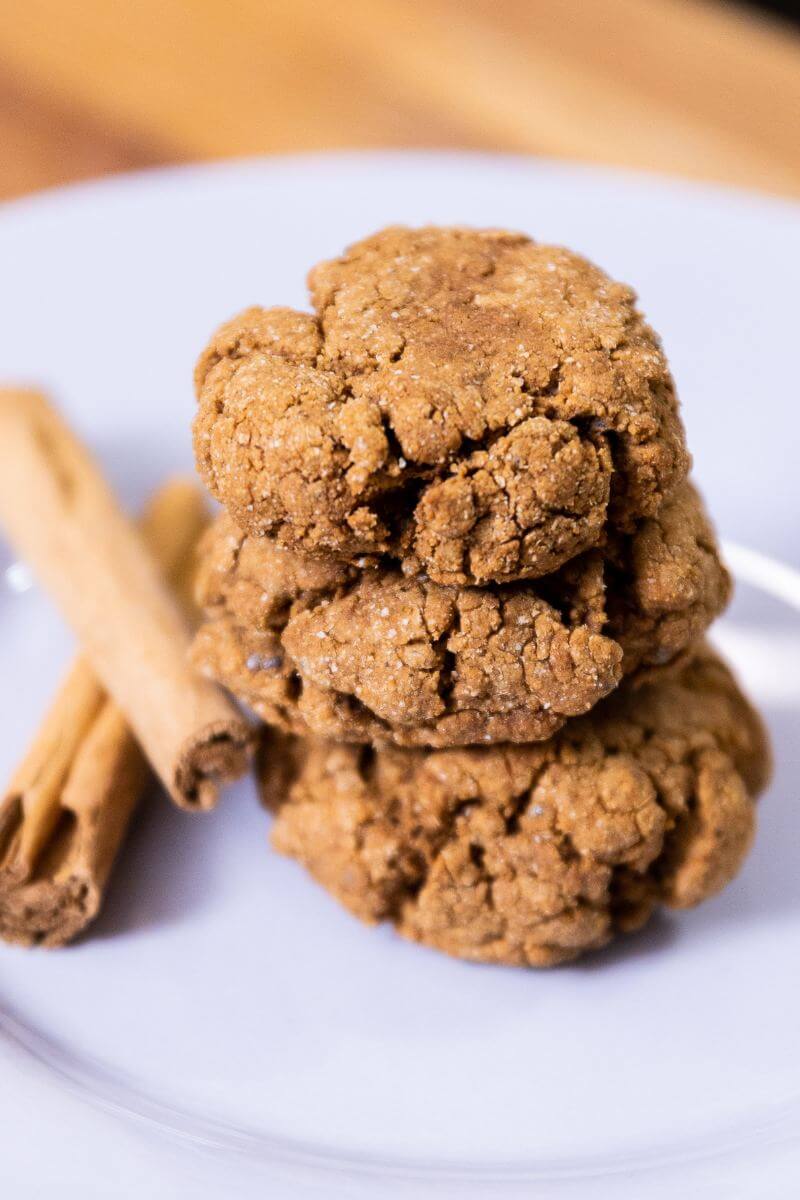 a stack of three vegan ginger molasses cookies on a plate next to a cinnamon stick