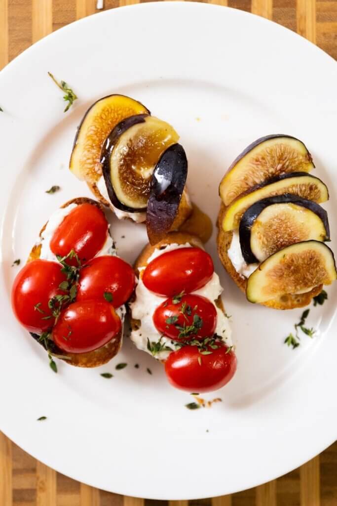 top view of whipped ricotta crostini on a large white plate with toppings