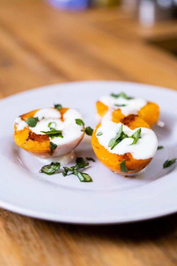 side view of glazed apricots on a plate topped with sauce