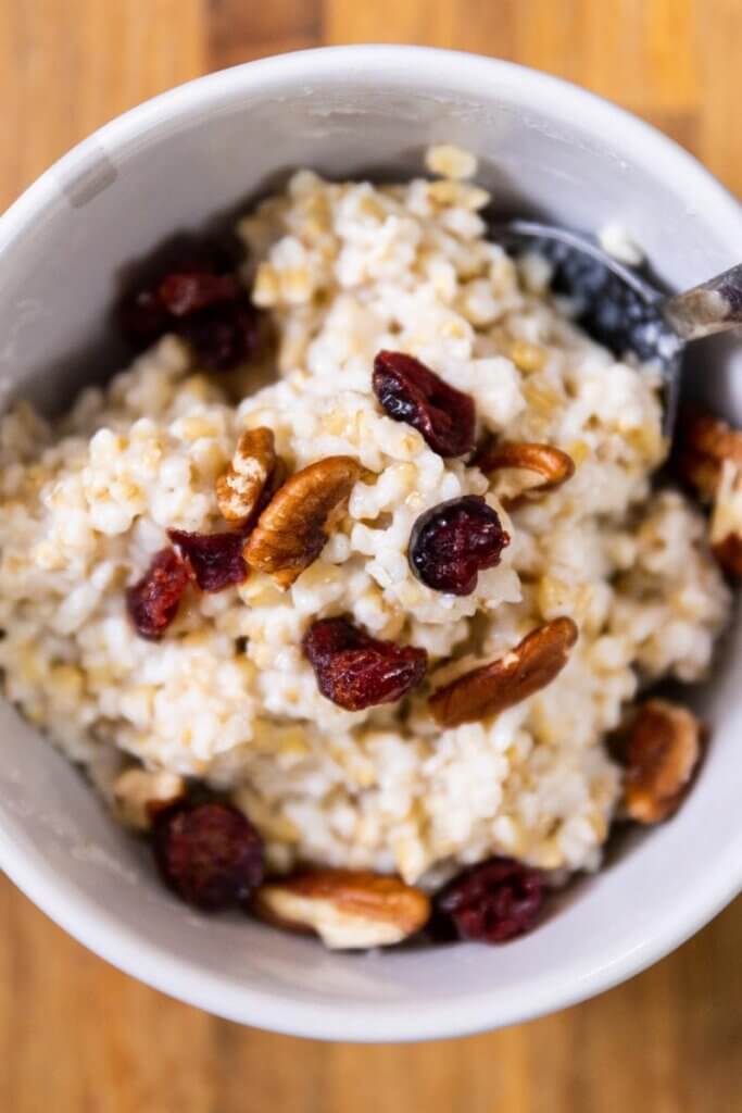 top view of coconut milk oatmeal in a white bowl with a spoon and toppings