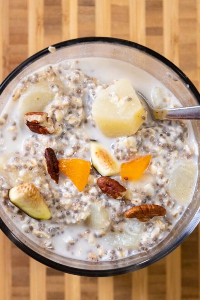 top view of pear overnight oats in a glass bowl with a spoon topped with nuts