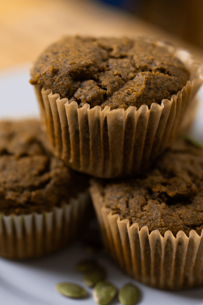 three buckwheat pumpkin muffins stacked on a white plate.