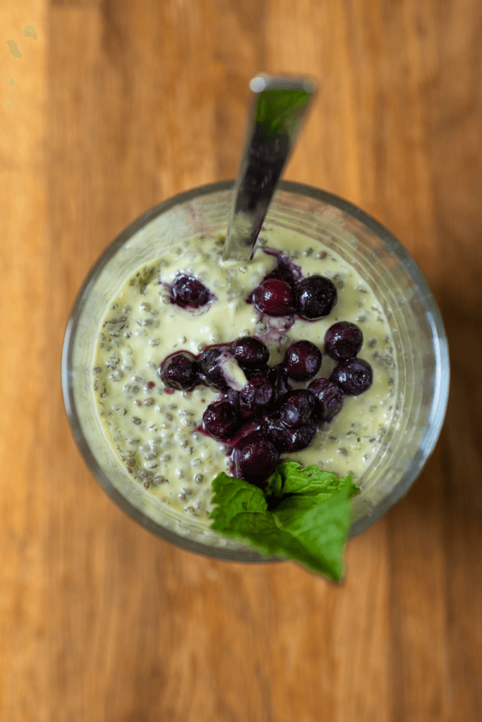 top view of avocado chia pudding in a glass with berries and mint, with a spoon stuck in. 