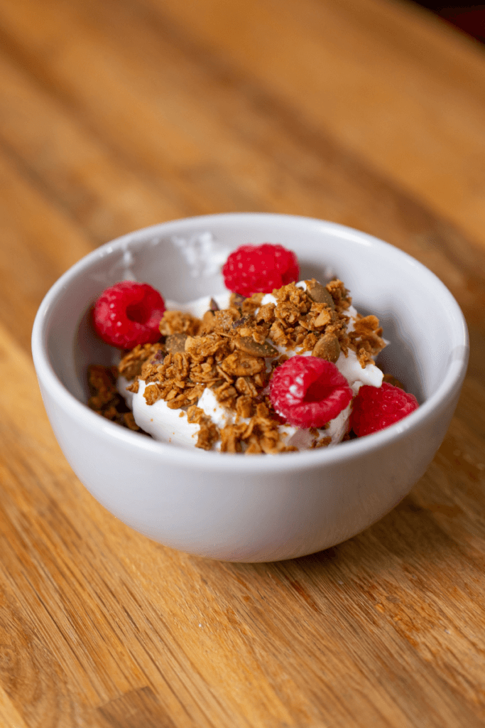 peanut butter granola in a bowl with yogurt and raspberries.