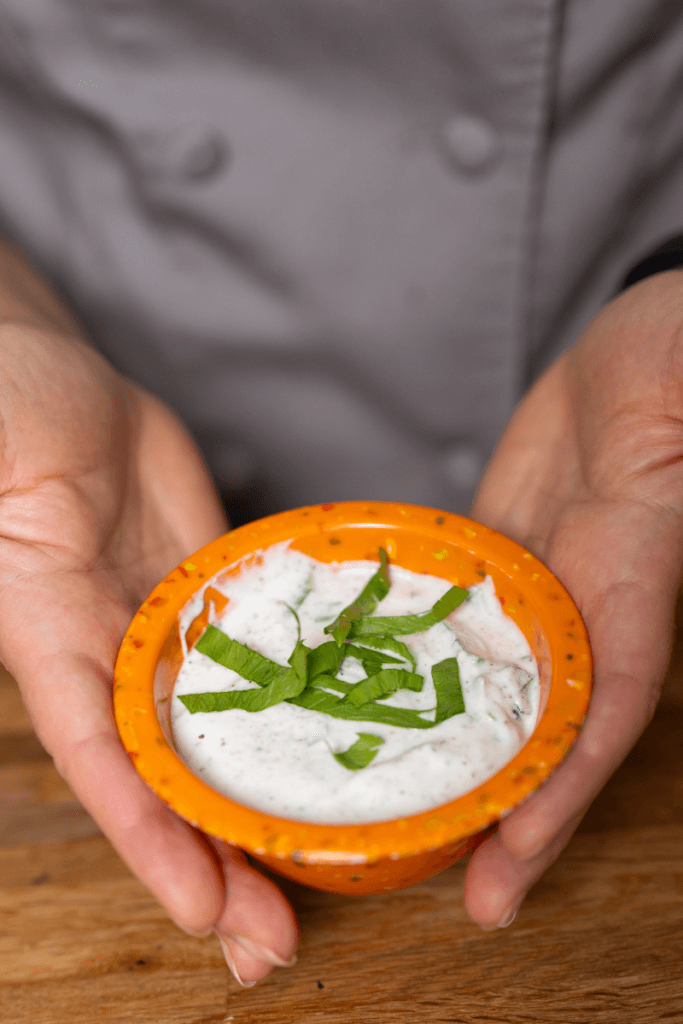 Holding a small orange bowl of homemade yogurt dressing.