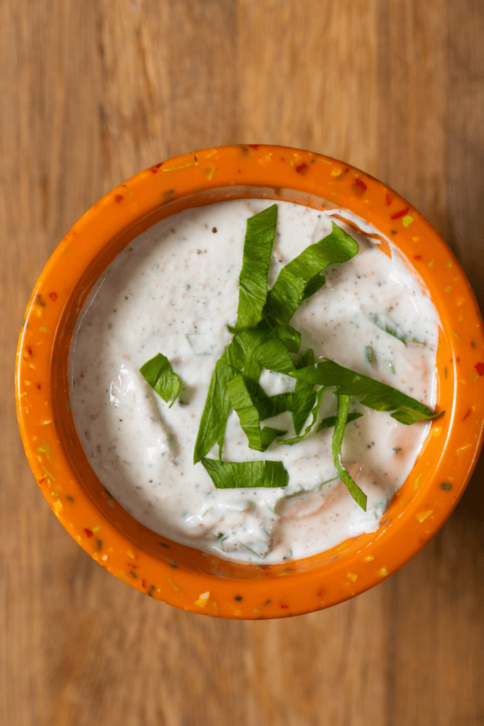 Top view of Greek yogurt ranch dressing topped with fresh basil in an orange bowl.