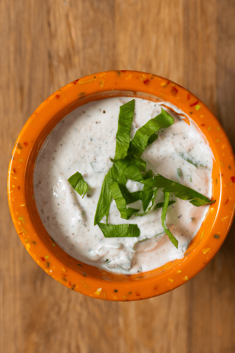 Top view of Greek yogurt ranch dressing topped with fresh basil in an orange bowl.