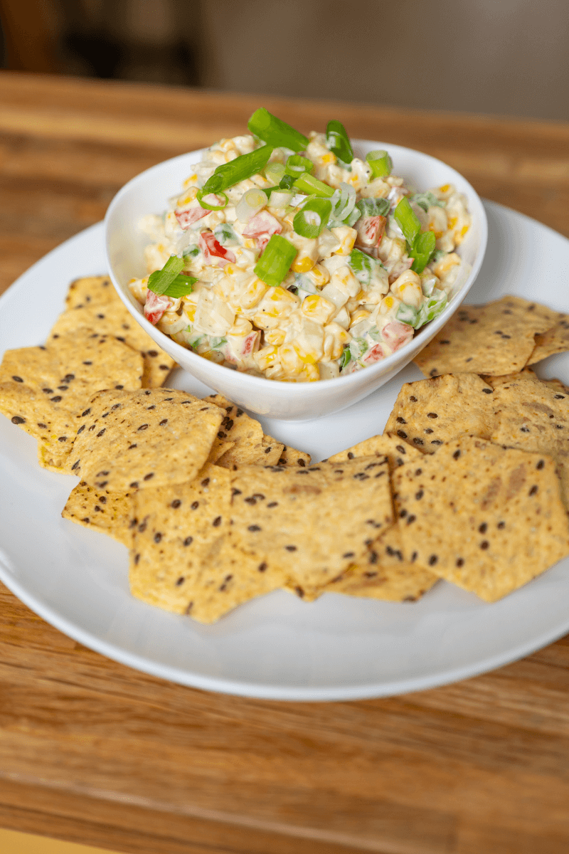 Cream cheese corn dip in a white bowl topped with scallions with crackers.