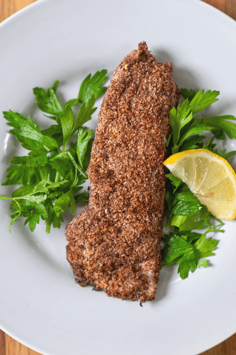 Pecan crusted halibut on a white plate with a lemon slice