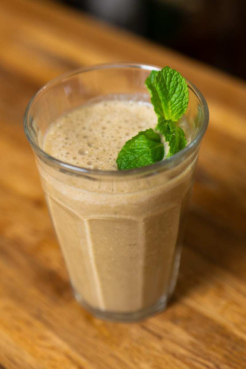 A mint chocolate chip smoothie in a glass with fresh mint leaves.