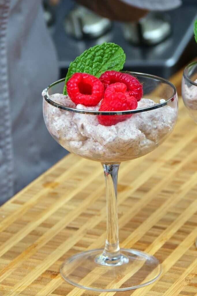 Chocolate ricotta mousse in a stemed glass topped with raspberries and mint.