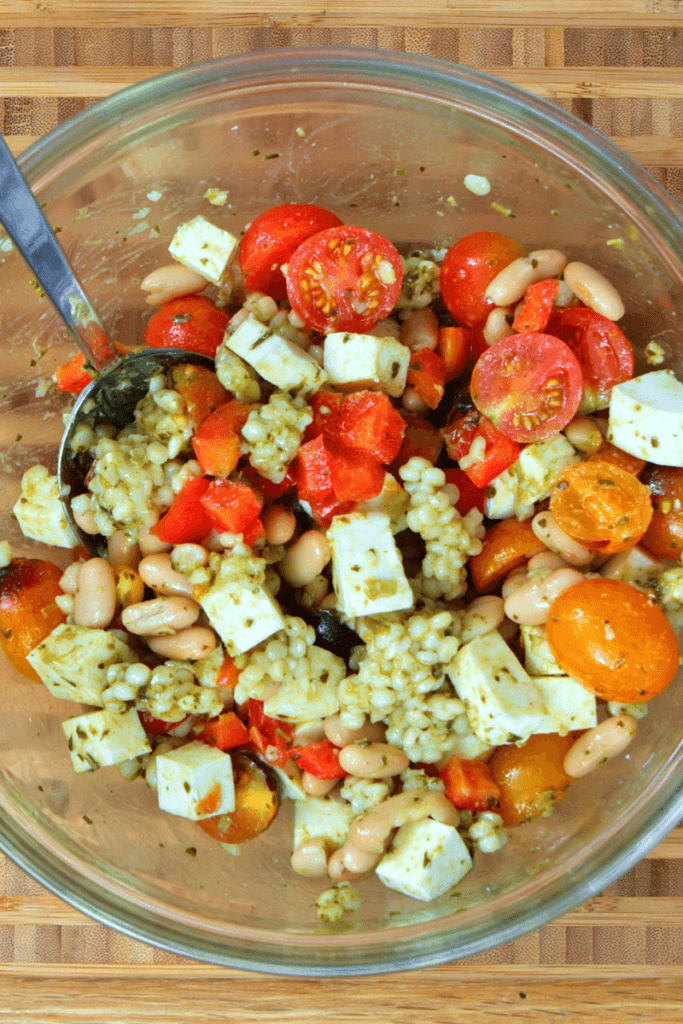 Top view of pesto cous cous in a glass mixing bowl.