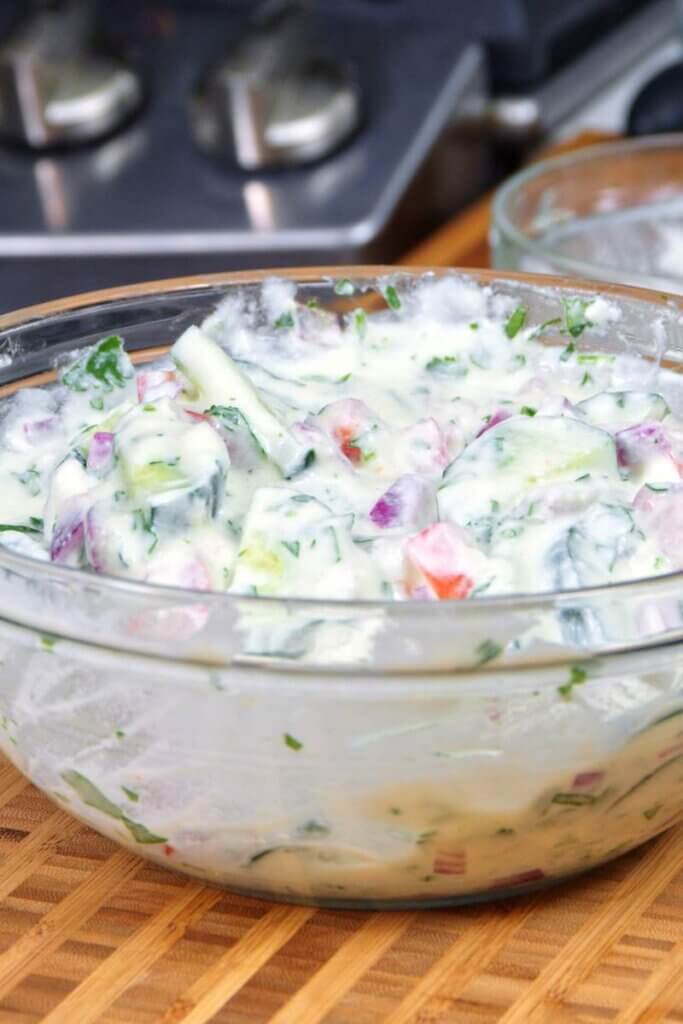 Creamy homemade kachumber raita in a glass mixing bowl on the counter.