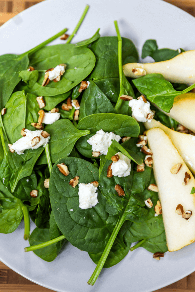 Pear and pecan salad with goat cheese on a white plate drizzled with homemade dressing.