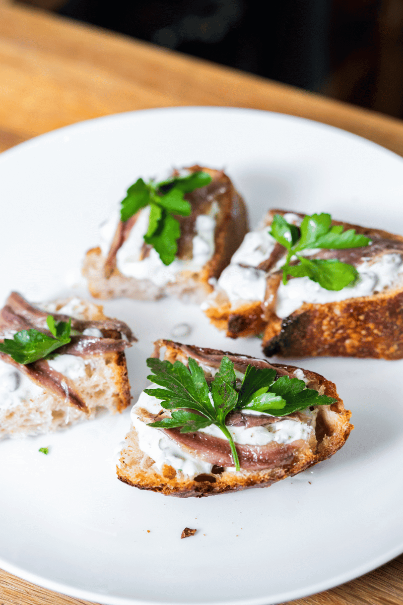 4 pieces of anchovy tapas on a white plate.