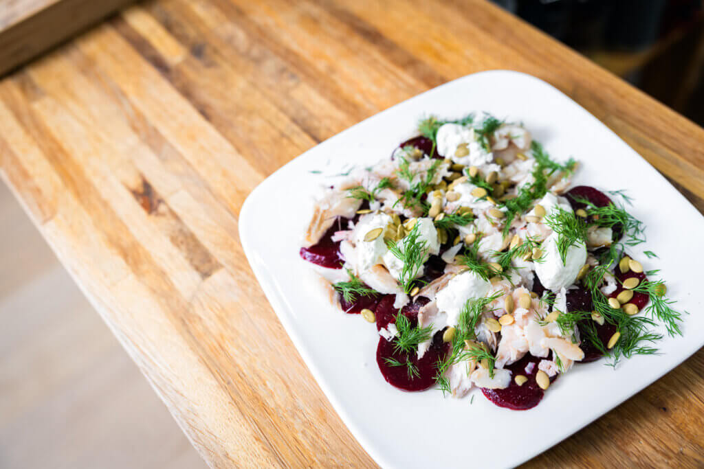 Smoked whitefish and beets on a white plate topped with sour cream, dill, and pumpkin seeds. 