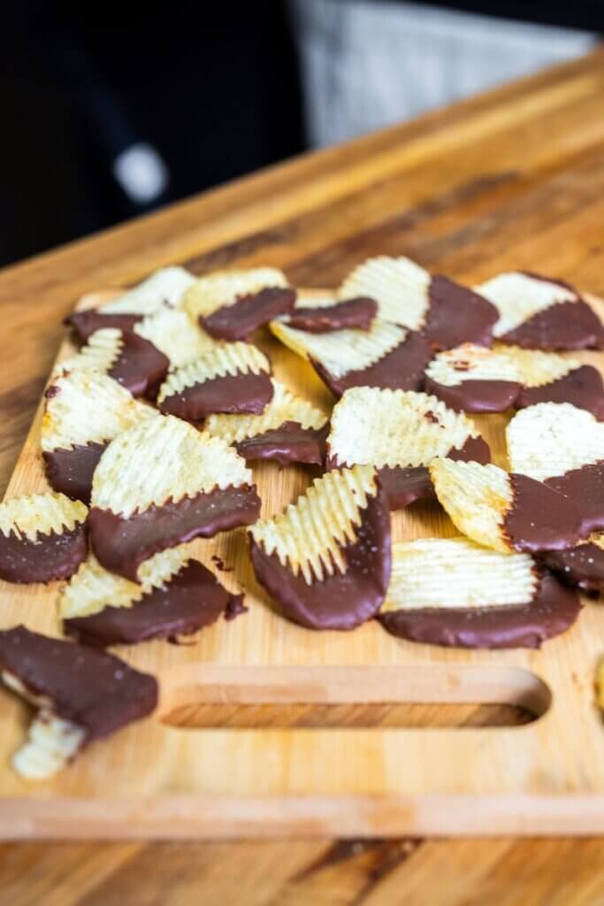 Chocolate covered potatoes chips on a wooden cutting board.