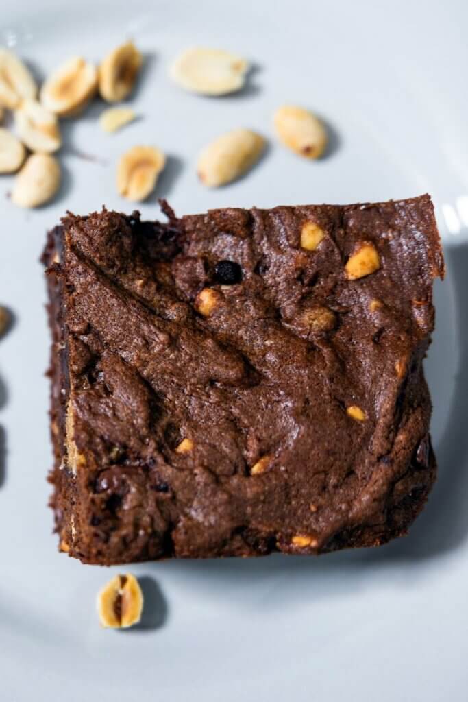Top view of a cocoa peanut butter brownie on a white plate next to peanuts.