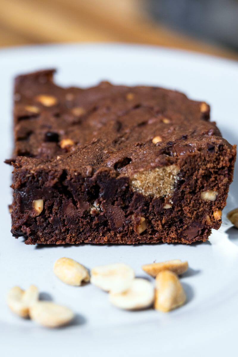 Homemade cocoa peanut butter brownie on a white plate next to peanuts.