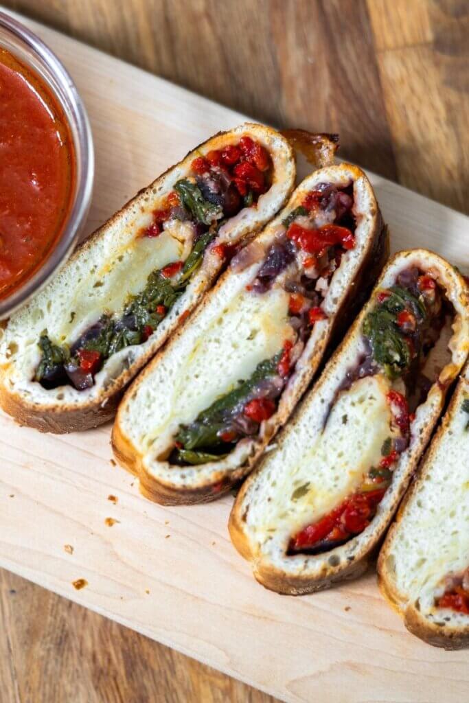 Sliced vegetable stromboli on a cutting board next to a bowl of marinara.