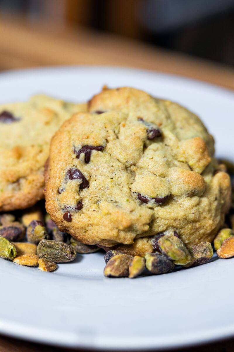 Pistachio chocolate chip cookies on a white plate with shelled pistachios on a plate.